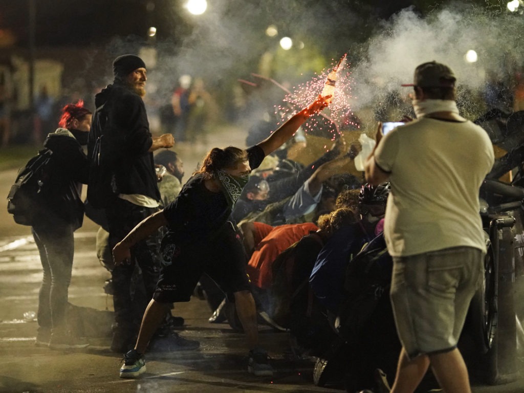 A protester thrusts an object toward police during clashes outside the courthouse late Tuesday during the third night of unrest in the city. CREDIT: David Goldman/AP