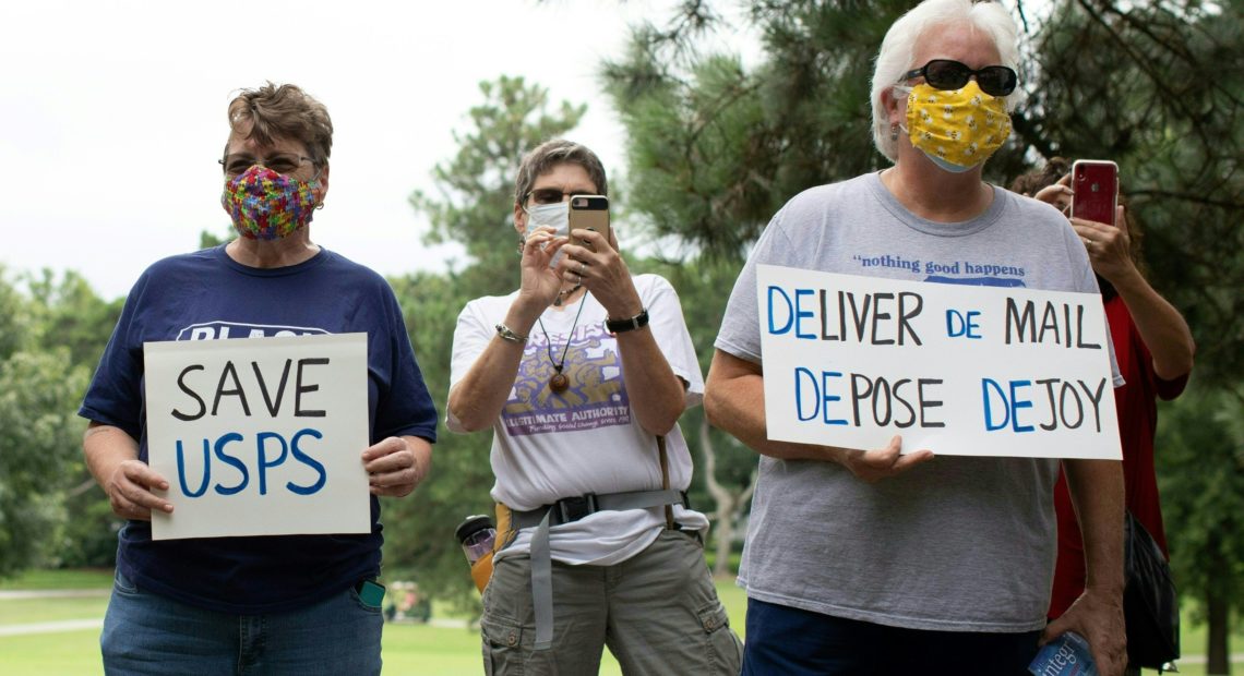 A group of protesters demonstrate in front of Postmaster General Louis DeJoy's home in Greensboro, N.C., on Sunday. Logan Cyrus/AFP via Getty Images