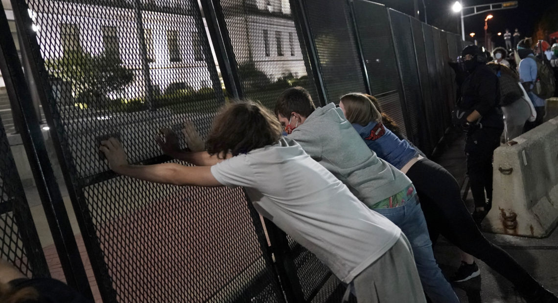 Protesters attempt to topple a fence outside the Kenosha County Courthouse late Tuesday in Kenosha, Wis. Protests continued following the police shooting of Jacob Blake on Sunday. CREDIT: David Goldman/AP