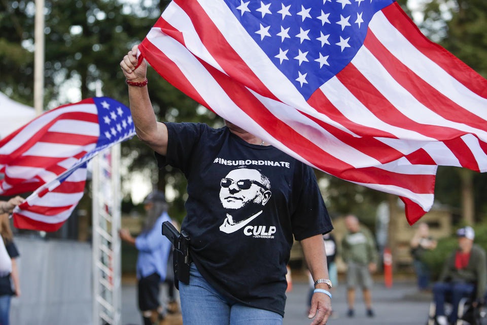 Cindy Sandland of Seattle waves a flag during a free rally and concert for Republican gubernatorial candidate Loren Culp in Arlington, Wash. on Aug. 22, 2020. CREDIT: Jason Redmond for Crosscut