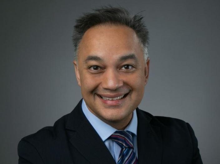 Portrait of a man in a black suit against a dark gray background. 