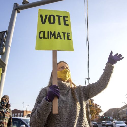 Kristin Green, left, and Kayla Bordelon, from the Citizens Climate Lobby, hold signs and wave to motorists on Election Day, Nov. 3, 2020, in Moscow, Idaho. CREDIT: Geoff Crimmins/The Moscow-Pullman Daily News via AP