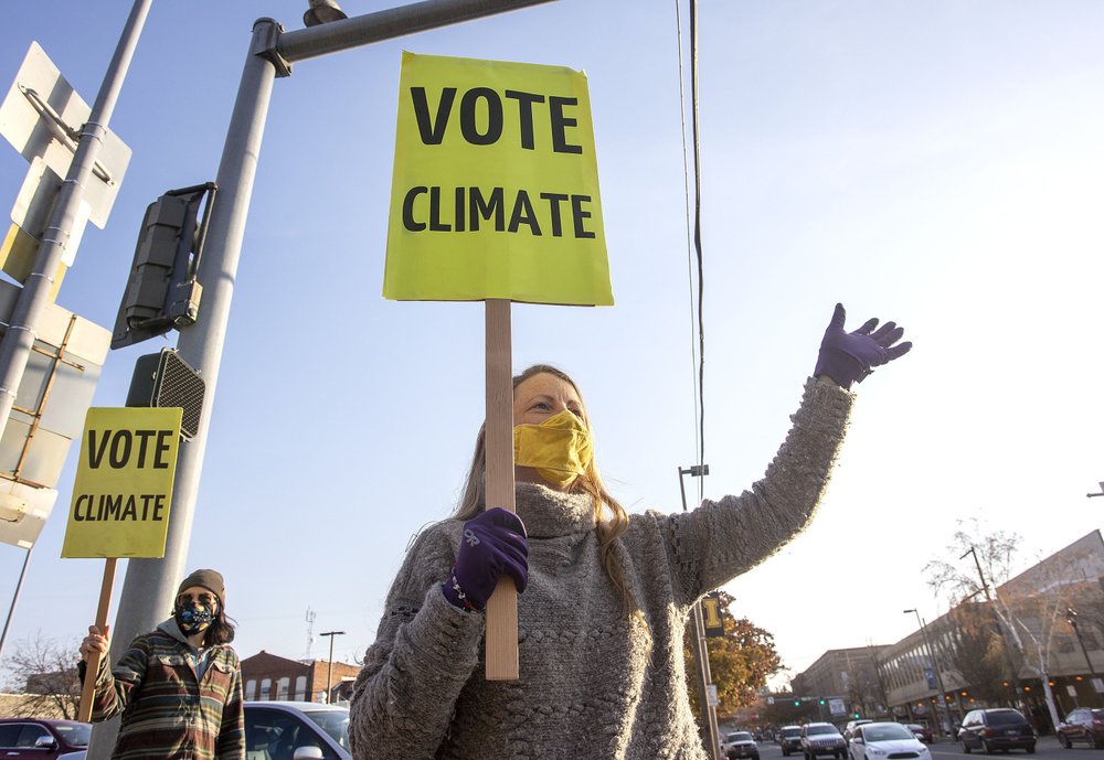 Kristin Green, left, and Kayla Bordelon, from the Citizens Climate Lobby, hold signs and wave to motorists on Election Day, Nov. 3, 2020, in Moscow, Idaho. CREDIT: Geoff Crimmins/The Moscow-Pullman Daily News via AP