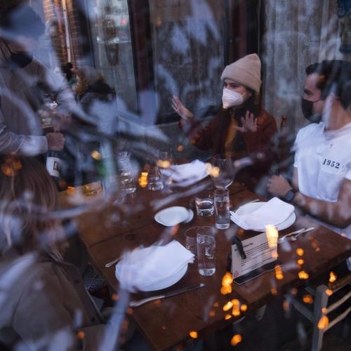 Server Luis Velez opens a bottle of wine for customers Mary Graf, left, Sophie Mandel and Andy Peraza, right, shown through a sheet of plastic surrounding the table, on Wednesday, October 21 , 2020, at Spinasse on Capitol Hill in Seattle.