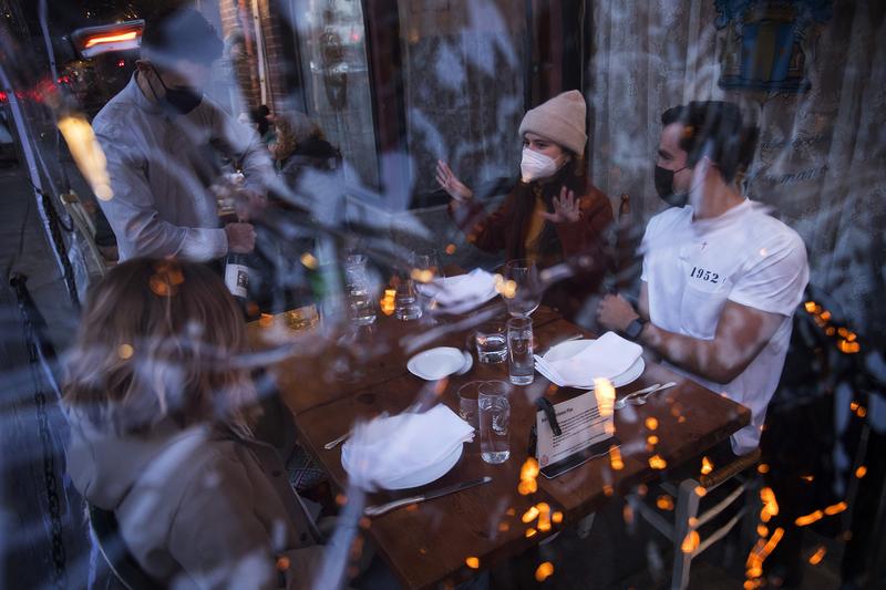 Server Luis Velez opens a bottle of wine for customers Mary Graf, left, Sophie Mandel and Andy Peraza, right, shown through a sheet of plastic surrounding the table, on Wednesday, October 21 , 2020, at Spinasse on Capitol Hill in Seattle.