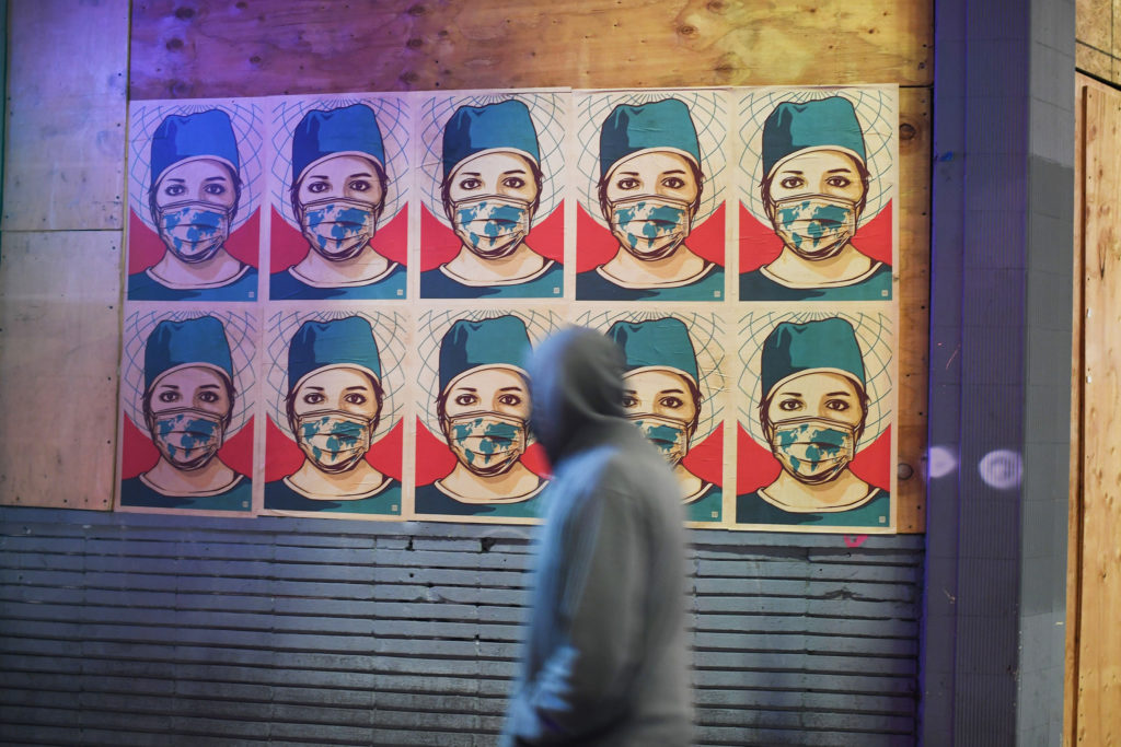 A pedestrian walks past posters showing a health care worker wearing a mask in Los Angeles. California became the second state to surpass 1 million coronavirus infections last week. CREDIT: Robyn Beck/AFP via Getty Images
