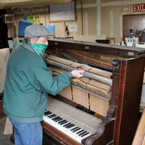 Michael Rohde disassembling a 120-year-old piano to salvage the metal and fine wood for other uses. CREDIT: Tom Banse/N3