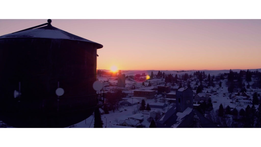 Drone shot of water tower and sun on horizon and snow covered town