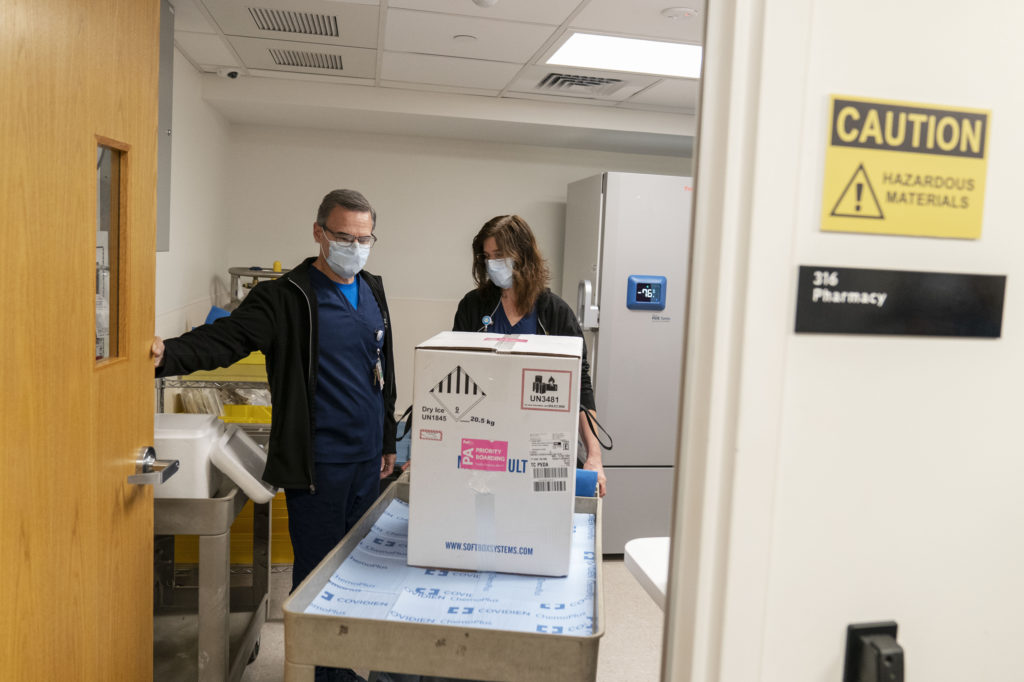 Pharmacists Richard Emery and Karen Nolan wheel a box containing the Pfizer-BioNTech COVID-19 vaccine next to a storage freezer as it arrives at Rhode Island Hospital in Providence, R.I, on Monday. CREDIT: David Goldman/AP