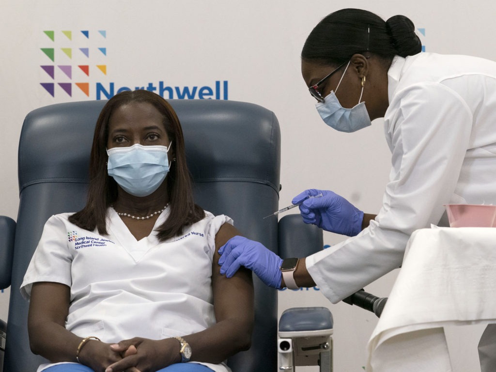 Sandra Lindsay (left) a nurse at Long Island Jewish Medical Center, is inoculated with the Pfizer-BioNTech COVID-19 vaccine by Dr. Michelle Chester on Monday in New York. CREDIT: Mark Lennihan/Pool/AP