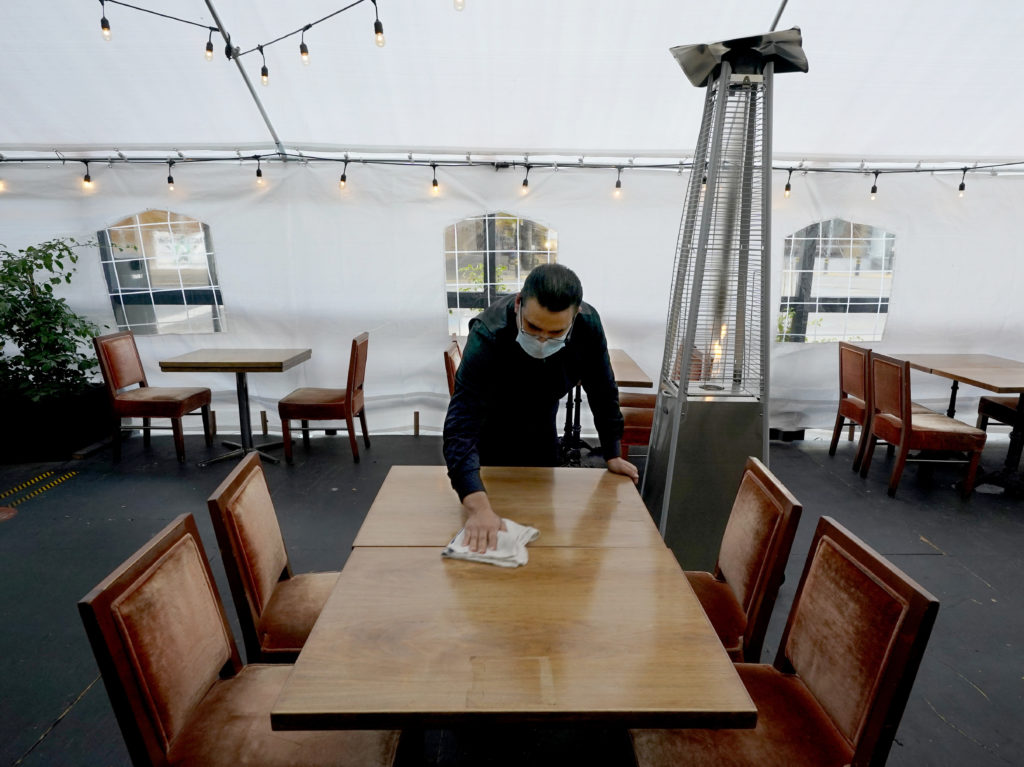 A person cleans a table in an outdoor tented dining area of a restaurant in Sacramento, Calif., on Nov. 19. Job growth slowed sharply in November as relief aid is due to expire at the end of the year. CREDIT: Rich Pedroncelli/AP