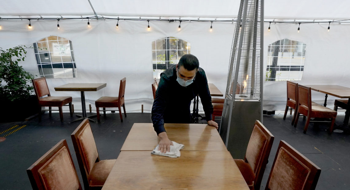 A person cleans a table in an outdoor tented dining area of a restaurant in Sacramento, Calif., on Nov. 19. Job growth slowed sharply in November as relief aid is due to expire at the end of the year. CREDIT: Rich Pedroncelli/AP