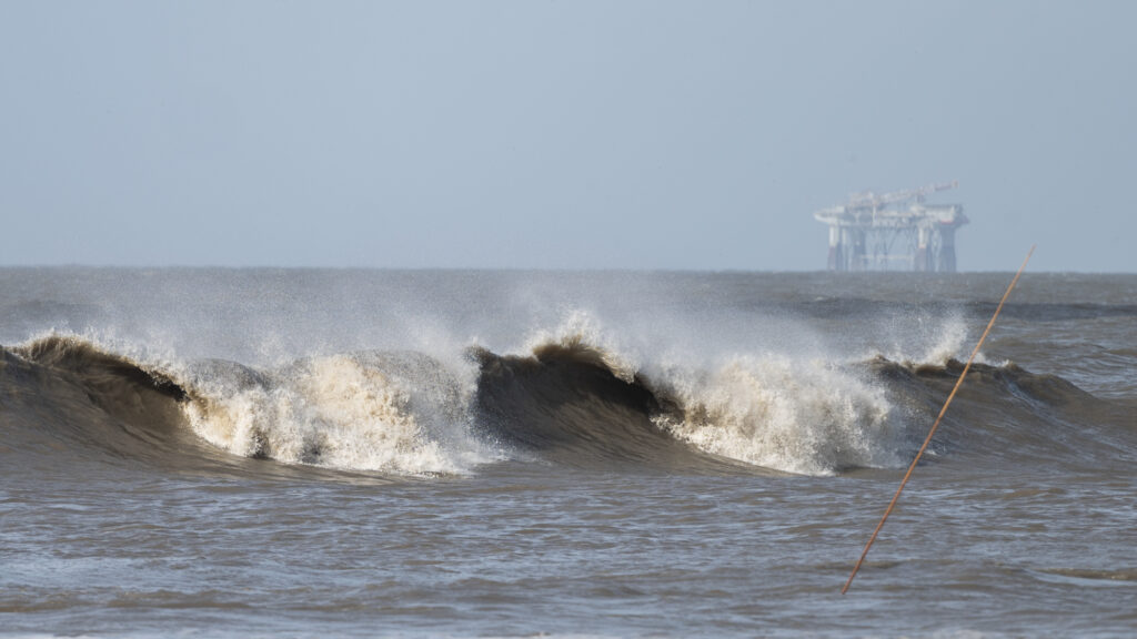 Hurricane Laura sends large waves crashing on a beach in Cameron, La., on Aug. 26 as an offshore oil rig appears in the distance. The most active hurricane season on record was just one of many challenges facing the oil industry this year — aside from the attention-grabbing crisis of the pandemic. CREDIT: Andrew Caballero-Reynolds/AFP via Getty Images