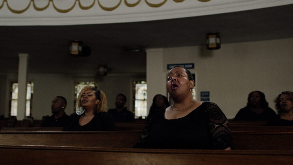 Ingrid Richardson singing in church, sitting in pew