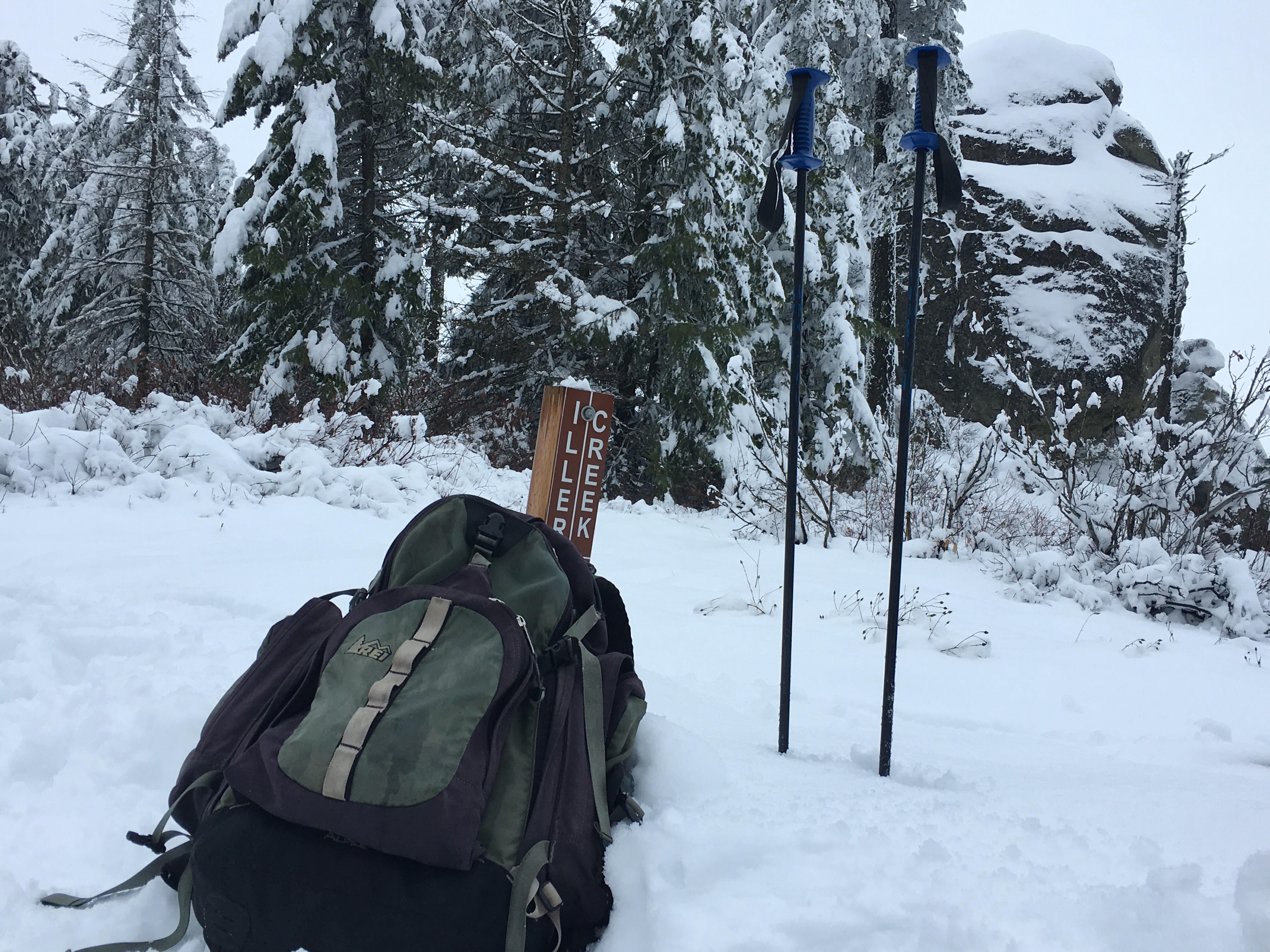 A backpack and hiking poles in the snow by a hiking trail sign in Spokane County's Dishman Hills