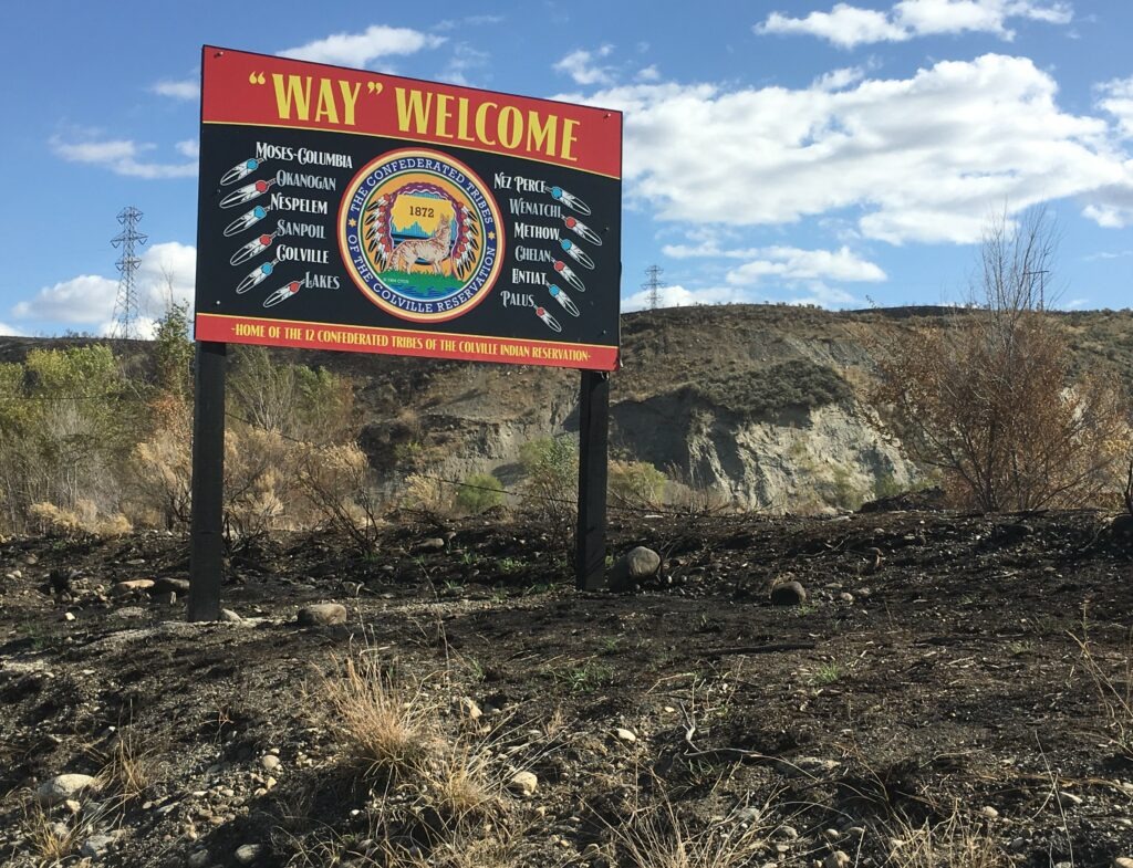 A welcome sign for the reservation of the Confederated Tribes of the Colville Reservation outside Omak Washington, with burned ground from the 2020 Cold Springs Fire