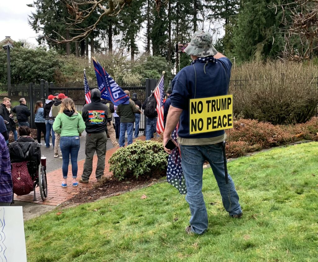 Pro-Trump protesters break through gate of Washington Governor's Residence on Jan. 6, 2021, with one person wearing a sign that reads "No Trump, No Peace."