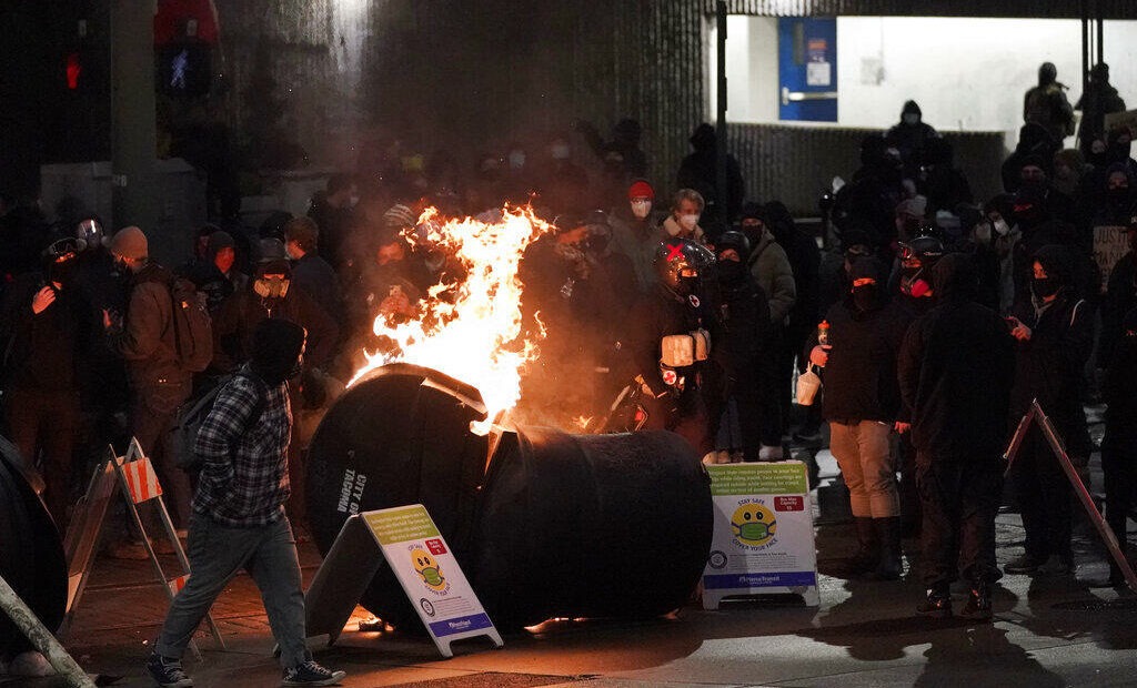 A trash can burns as people take part in a protest against police brutality, late Sunday, Jan. 24, 2021, in downtown Tacoma, Wash., south of Seattle. The protest came a day after at least two people were injured when a Tacoma Police officer responding to a report of a street race drove his car through a crowd of pedestrians that had gathered around him. Several people were knocked to the ground and at least one person was run over. CREDIT: Ted S. Warren/AP
