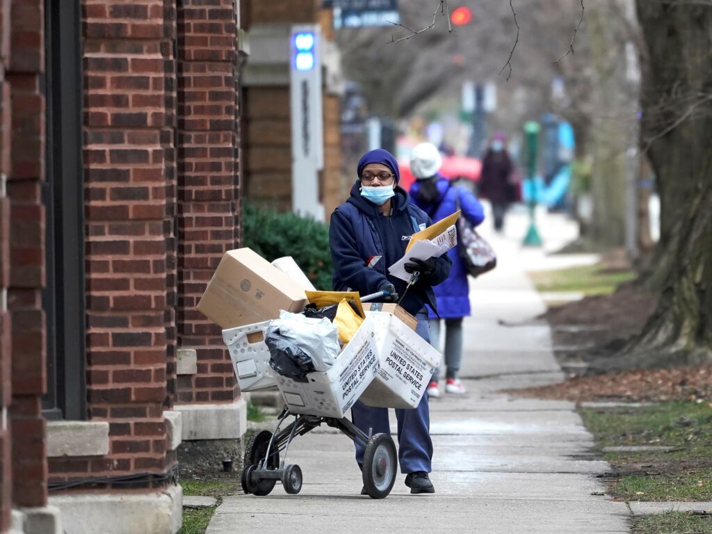 A U.S. postal worker delivers packages, boxes and letters in Chicago's Hyde Park neighborhood shortly before Christmas. The U.S. Postal Service said it faces "unprecedented volume increases and limited employee availability due to the impacts of COVID-19." Charles Rex Arbogast/AP