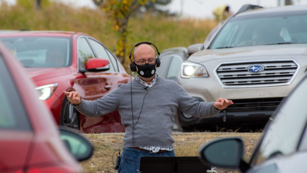 Shantz conducts Luminous Voices' first car concert, on Oct. 4, 2020. Audience vehicles are seen parked to behind him. CREDIT: Kenton Smith