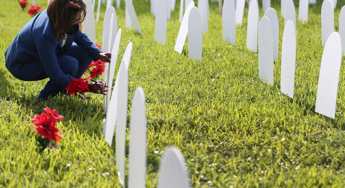 Mary Estime-Irvin, a councilwoman in North Miami, Fla., writes the name of a friend lost to COVID-19 on a symbolic tombstone that is part of a pandemic memorial at Griffing Park in North Miami in October. CREDIT: Joe Raedle/Getty Images