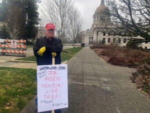 John Hess holding a sign describing President Joe Biden as a “traitor” and a “thief," as he stands outside a barricade set up by state troopers at the Washington state Capitol building, Jan. 20, 2021. CREDIT: Melissa Santos/Crosscut