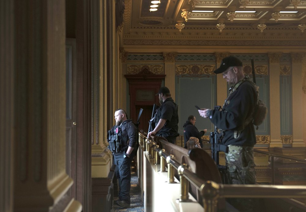 In this April 30, 2020 photo, armed members of a militia group watch the protest outside while waiting for the Michigan Senate to vote at the Capitol in Lansing, Mich. CREDIT: Nicole Hester/MLive.com/Ann Arbor News via AP File