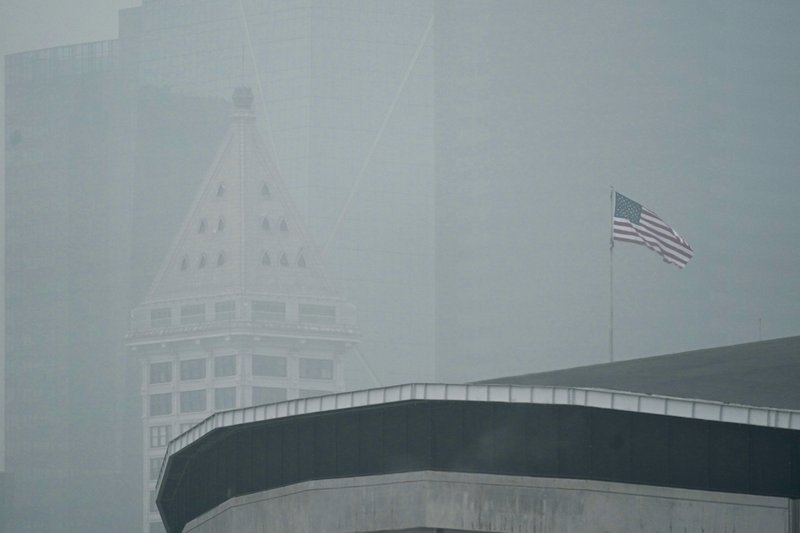 In this Sept. 14, 2020 photo, a U.S. flag flies near Smith Tower in downtown Seattle as air thick with smoke from wildfires as seen over CenturyLink Field. The damage caused by wildfires can be devastating, yet researchers say the smoke from the annually recurring blazes also delivers economic damage to areas that were never touched by the flames. CREDIT: Ted S. Warren/AP