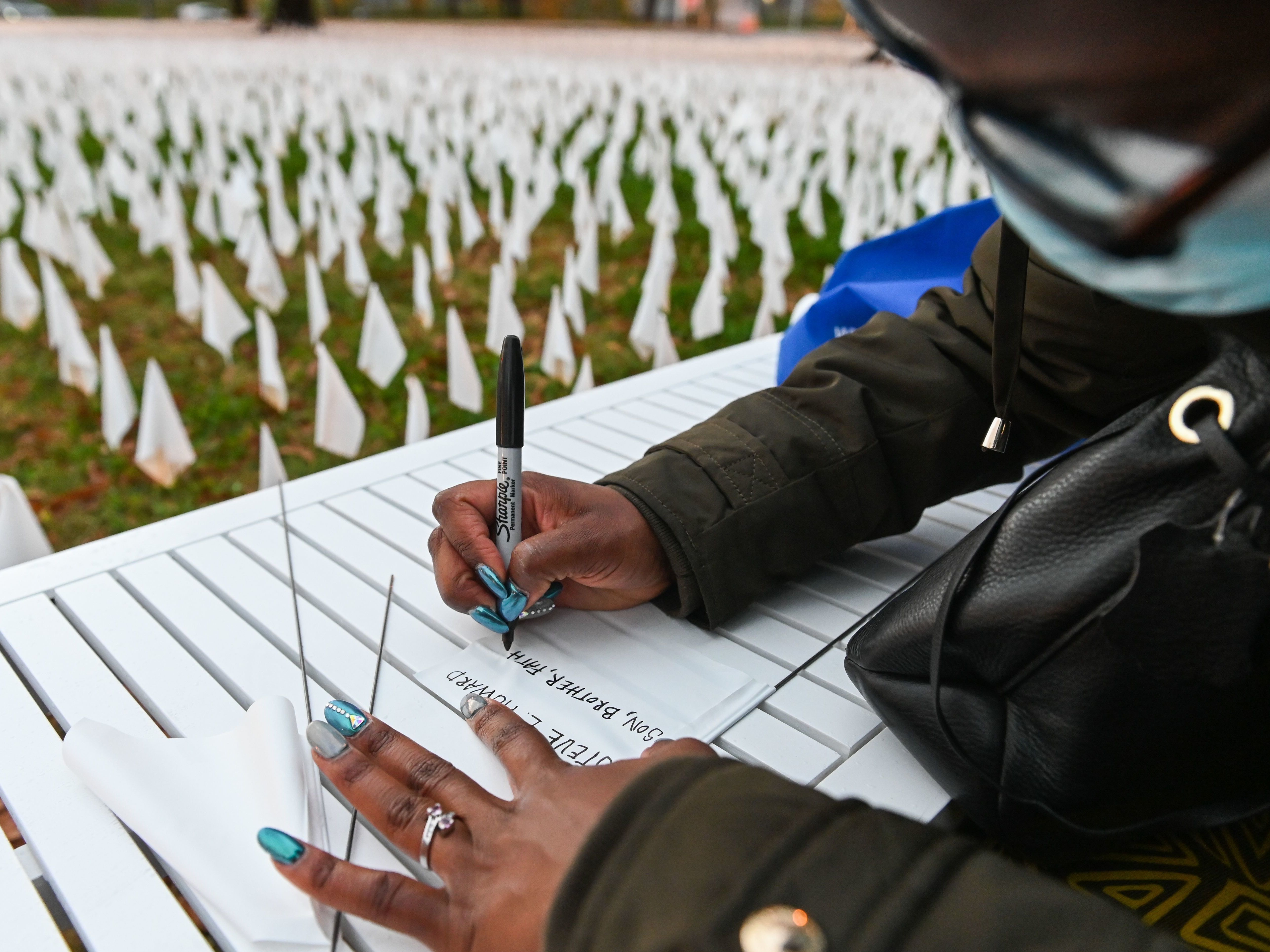 Patrice Howard writes on white flags before planting them to remember her recently deceased father and close friends in November at "IN AMERICA How Could This Happen...," a public art installation in Washington, D.C. Led by artist Suzanne Firstenberg, volunteers planted white flags in a field to symbolize each life lost to COVID-19 in the U.S. CREDIT: Roberto Schmidt/AFP via Getty Images