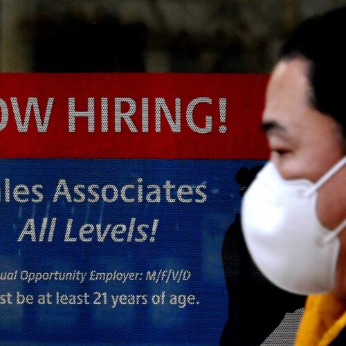 A man walks past a "Now Hiring" sign in front of a store in early December in Arlington, Va. U.S. employers added 379,000 jobs in February, as hiring picked up sharply from the previous month. CREDIT: Olivier Douliery/AFP via Getty Images