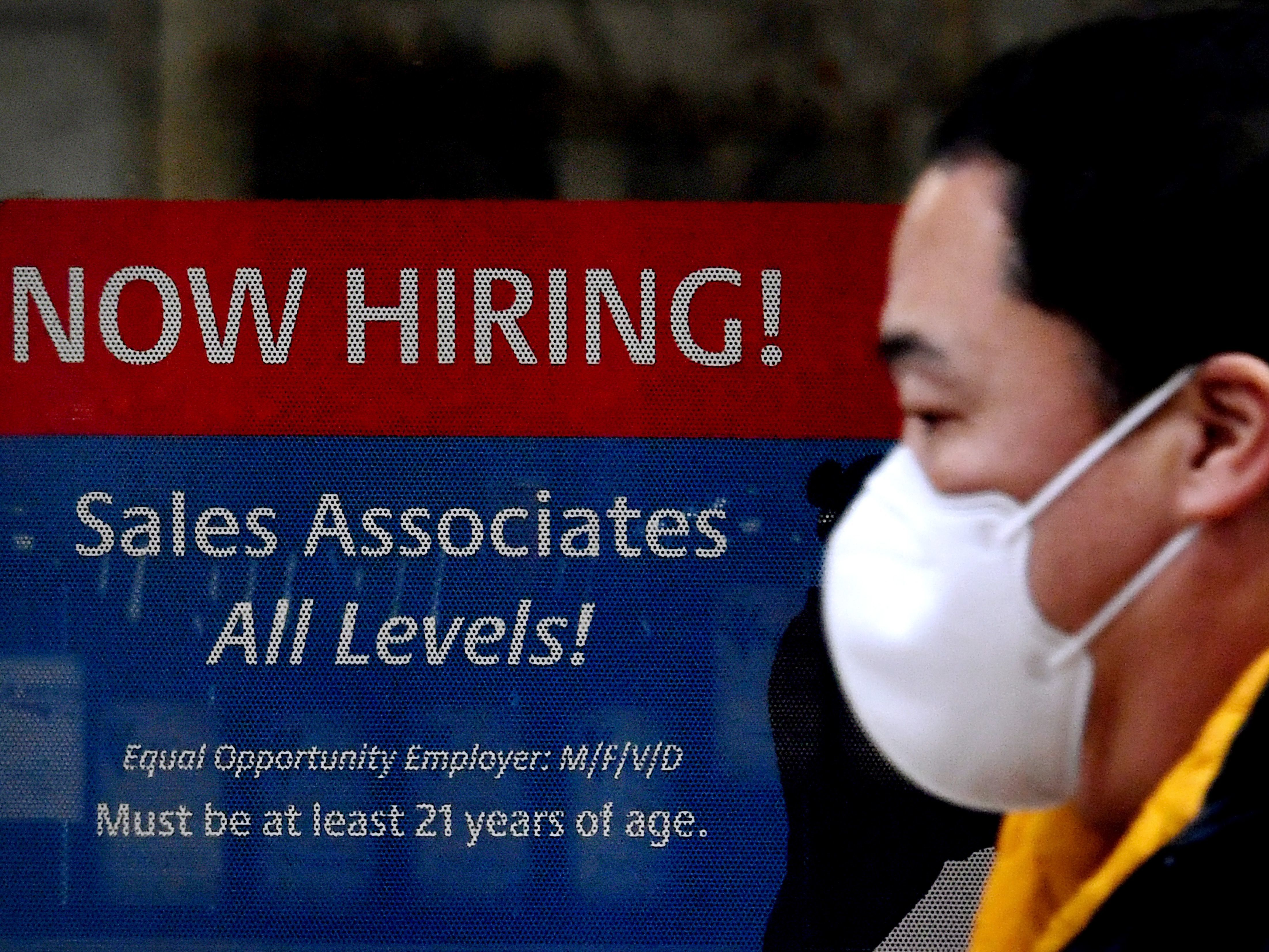 A man walks past a "Now Hiring" sign in front of a store in early December in Arlington, Va. U.S. employers added 379,000 jobs in February, as hiring picked up sharply from the previous month. CREDIT: Olivier Douliery/AFP via Getty Images