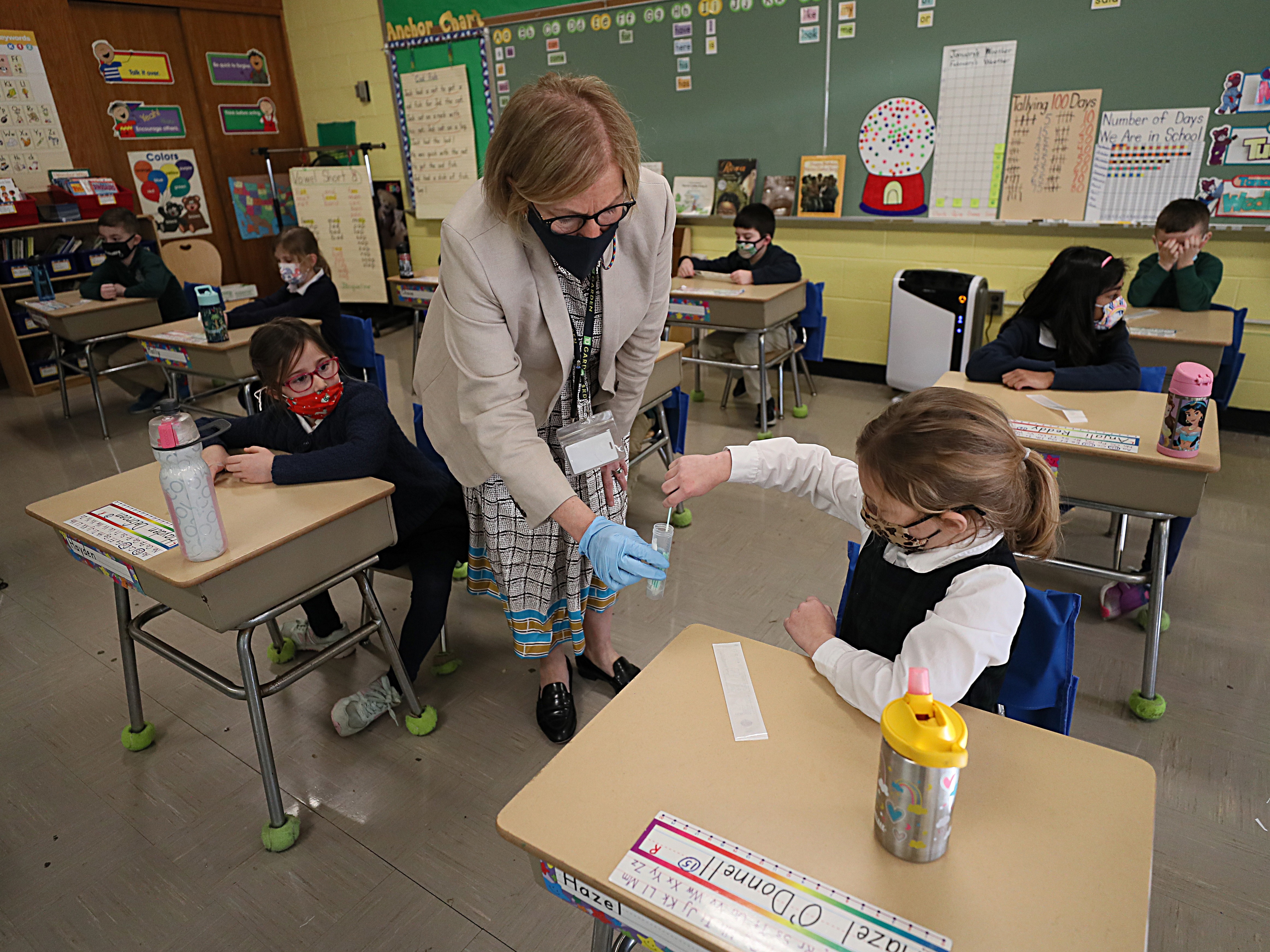 A student gives her coronavirus swab to Helenann Civian, the principal of South Boston Catholic Academy in Boston in January. The White House announced $10 billion to expand testing in K-12 schools. CREDIT: Suzanne Kreiter/Boston Globe via Getty Images