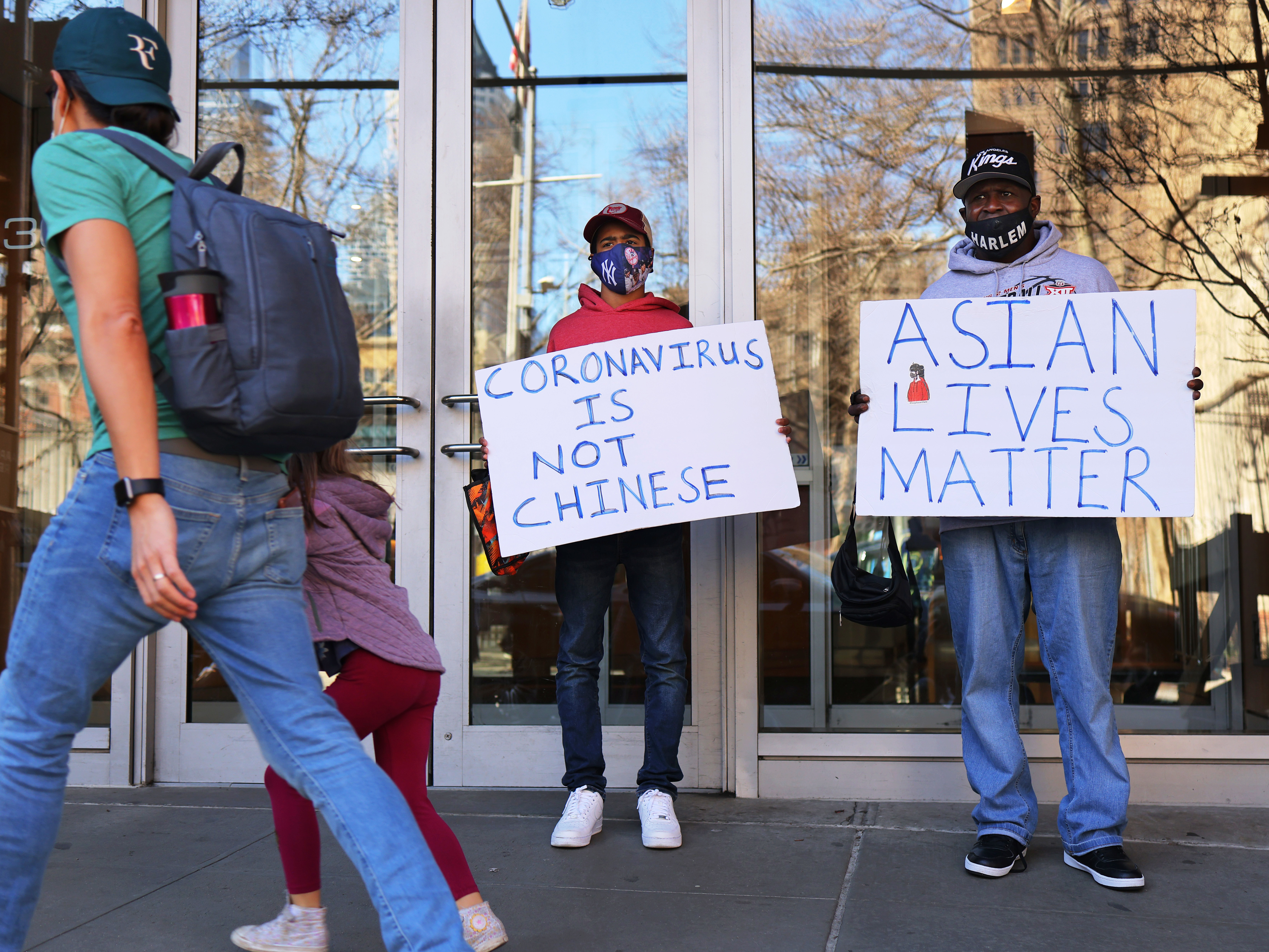 Cameron Hunt and his father, Calvin Hunt, hold signs of support on Tuesday outside the West 43rd Street apartment building in Manhattan where a man physically and verbally attacked a 65-year-old Asian American woman on Monday in an incident that police are investigating as a hate crime. CREDIT: Michael M. Santiago/Getty Images