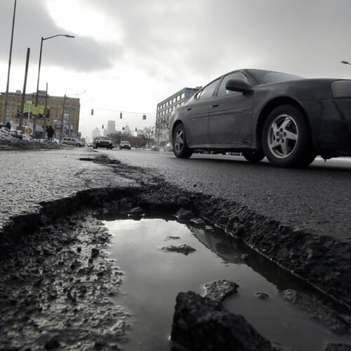 In this Feb. 11, 2014 photo a car drives by a pothole in Detroit. The relentless cycle of snow and bitter cold this winter is testing the skeletons of steel and cement on which communities are built. Pipes are bursting in towns that are not used to such things, and roads are turning into moonscapes of gaping potholes big enough to snap axles of passing vehicles. (AP Photo/Carlos Osorio)