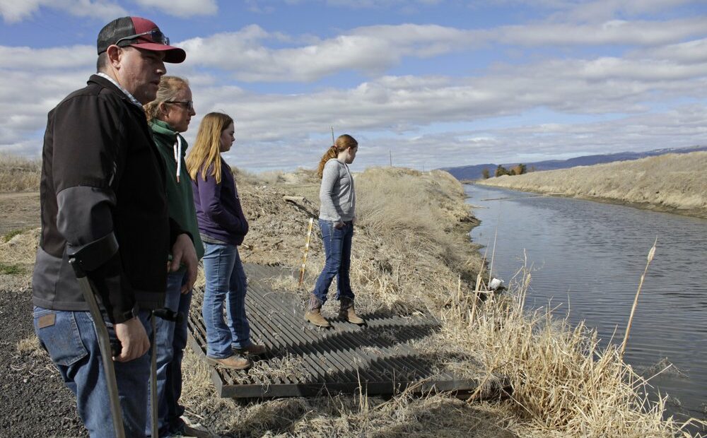 File photo, March 2, 2020: Farmer Ben DuVal with his wife, Erika, and their daughters, Hannah, third from left, and Helena, fourth from left, stand near a canal for collecting run-off water near their property in Tulelake, Calif. Federal officials announced in April 2021 that farmers who rely on a massive irrigation project spanning the Oregon-California border will get 8% of the deliveries they need amid a severe drought. CREDIT: Gillian Flaccus/AP