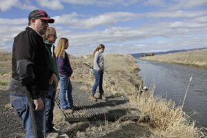 File photo, March 2, 2020: Farmer Ben DuVal with his wife, Erika, and their daughters, Hannah, third from left, and Helena, fourth from left, stand near a canal for collecting run-off water near their property in Tulelake, Calif. Federal officials announced in April 2021 that farmers who rely on a massive irrigation project spanning the Oregon-California border will get 8% of the deliveries they need amid a severe drought. CREDIT: Gillian Flaccus/AP
