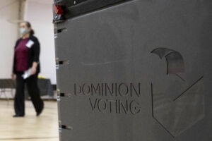 A worker passes a Dominion Voting Systems ballot scanner during Georgia's runoff Senate elections in January in Gwinnett County outside Atlanta. Former President Donald Trump and his allies spread falsehoods about the company's role in the 2020 election, leading to a slew of defamation lawsuits. Ben Gray/AP