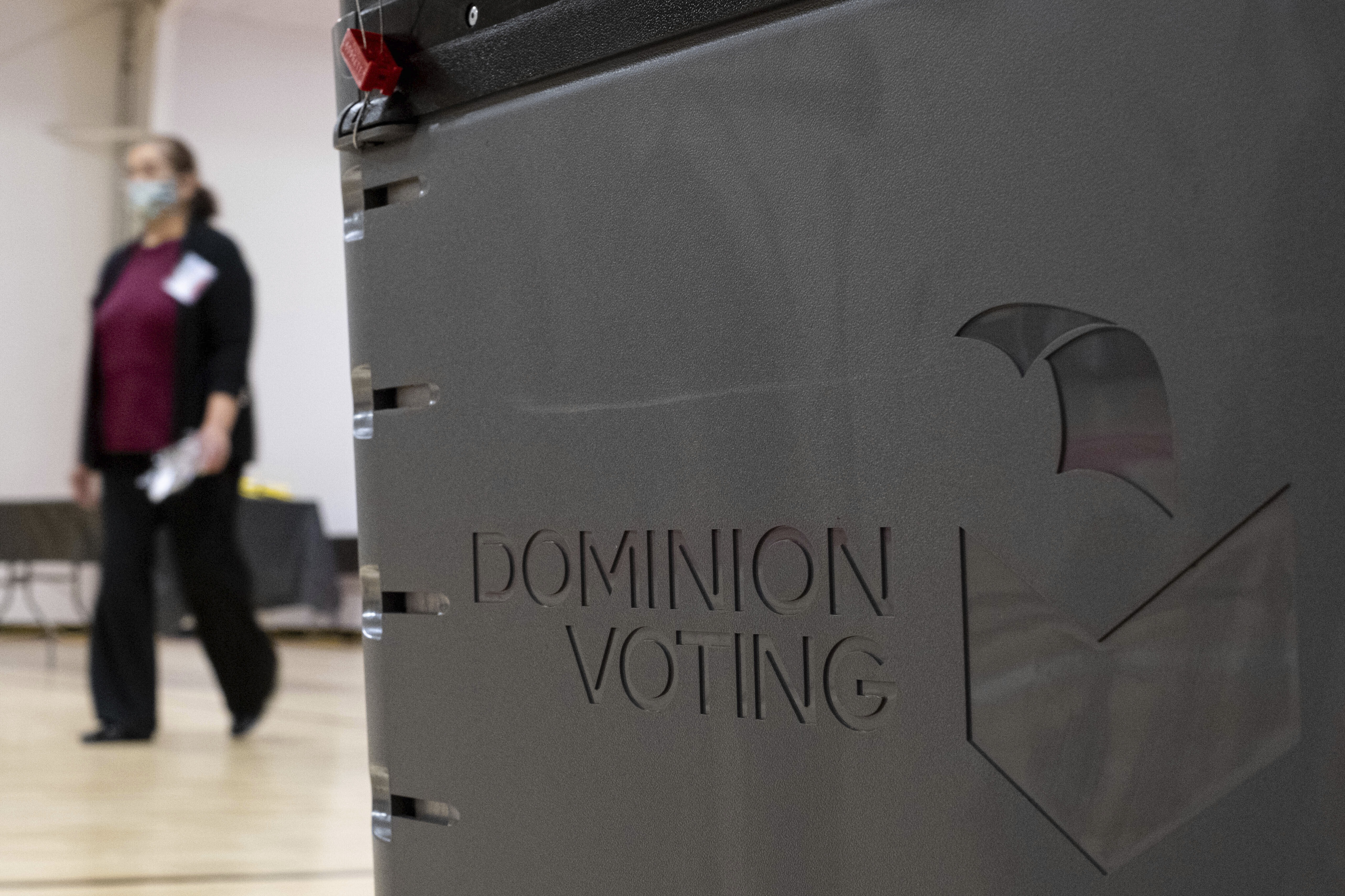 A worker passes a Dominion Voting Systems ballot scanner during Georgia's runoff Senate elections in January in Gwinnett County outside Atlanta. Former President Donald Trump and his allies spread falsehoods about the company's role in the 2020 election, leading to a slew of defamation lawsuits. Ben Gray/AP