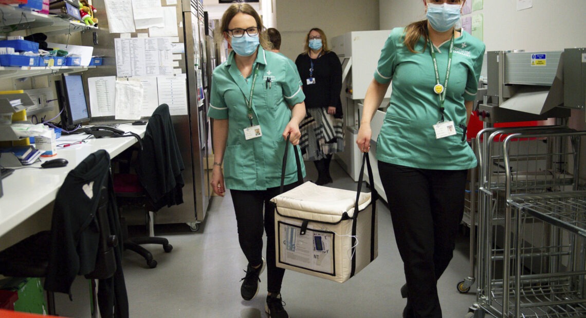 On Wednesday, pharmacists at the West Wales General Hospital in Carmarthen, Wales, transport a cool box containing the first batch of Moderna vaccines being distributed in Britain. CREDIT: Jacob King/AP