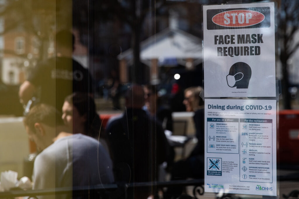 A sign requiring face masks and COVID-19 protocols is displayed at a restaurant in Plymouth, Mich., on March 21. Coronavirus cases in Michigan are skyrocketing after months of steep declines, one sign that a new surge may be starting. CREDIT: Emily Elconin/Bloomberg via Getty Images