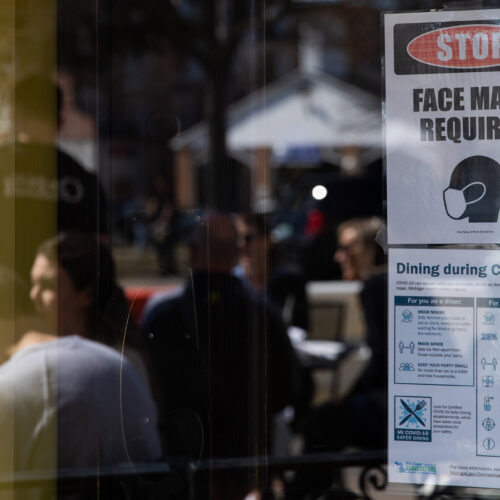A sign requiring face masks and COVID-19 protocols is displayed at a restaurant in Plymouth, Mich., on March 21. Coronavirus cases in Michigan are skyrocketing after months of steep declines, one sign that a new surge may be starting. CREDIT: Emily Elconin/Bloomberg via Getty Images