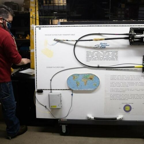 Michael Moore, an information technology construction coordinator, is seen with an explanatory board about telecommunications services at a co-location data center inside Grays Harbor Pubic Utility District's headquarters in Aberdeen on March 4, 2021. Two bills approved by Washington's Legislature would let public utility districts offer broadband to retail customers. But there's some confusion about how the bills would interact. CREDIT: Matt M. McKnight/Crosscut