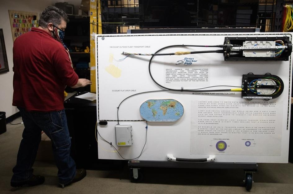 Michael Moore, an information technology construction coordinator, is seen with an explanatory board about telecommunications services at a co-location data center inside Grays Harbor Pubic Utility District's headquarters in Aberdeen on March 4, 2021. Two bills approved by Washington's Legislature would let public utility districts offer broadband to retail customers. But there's some confusion about how the bills would interact. CREDIT: Matt M. McKnight/Crosscut