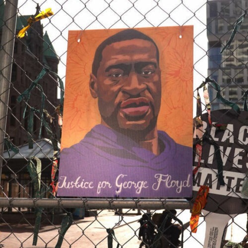 A picture of George Floyd hangs on a fence barrier that surrounds the Hennepin County Government Center in Minneapolis during the trial of former police officer Derek Chauvin in March. The Justice Department is now bringing criminal charges against Chauvin over allegedly violating Floyd's rights and using excessive force in restraining him. CREDIT: Scott Olson/Getty Images