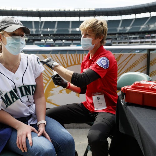 Sydney Porter of Bellevue, Wash., receives her COVID-19 vaccination from Kristine Gill, with the Seattle Fire Department's Mobile Vaccination Teams, before the game between the Seattle Mariners and the Baltimore Orioles at T-Mobile Park on May 5 in Seattle. A late spring COVID-19 surge has filled hospitals in the metro areas around Seattle. CREDIT: Steph Chambers/Getty Images