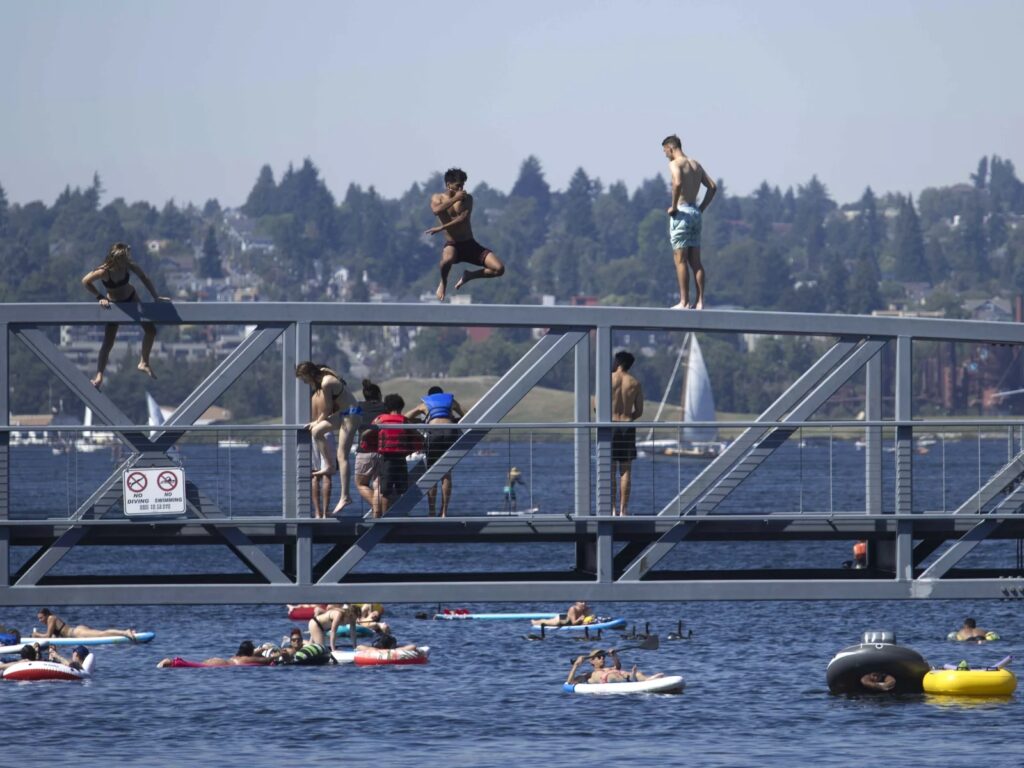 People jump from a pedestrian bridge at Lake Union Park in Seattle on Sunday as a record-setting heat wave blasts the Pacific Northwest. CREDIT: John Froschauer/AP