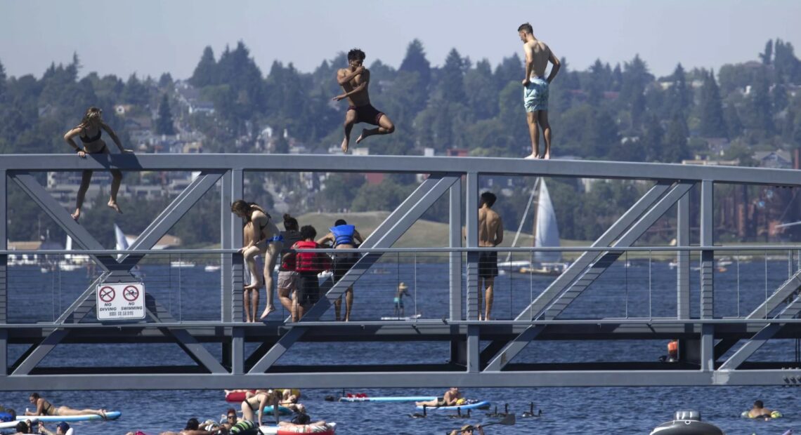 People jump from a pedestrian bridge at Lake Union Park in Seattle on Sunday as a record-setting heat wave blasts the Pacific Northwest. CREDIT: John Froschauer/AP