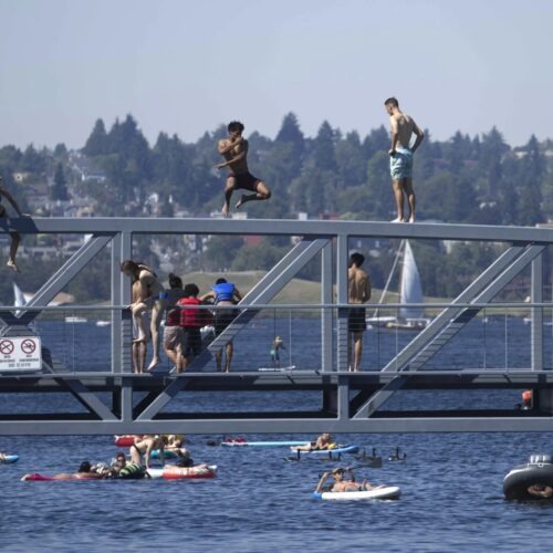 People jump from a pedestrian bridge at Lake Union Park in Seattle on Sunday as a record-setting heat wave blasts the Pacific Northwest. CREDIT: John Froschauer/AP