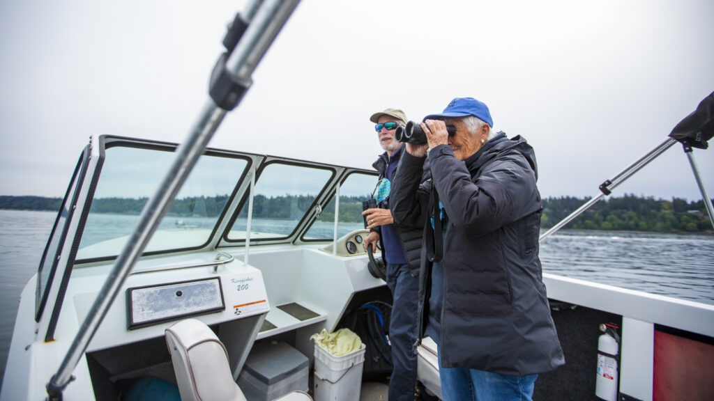 Naturalist Jill Hein (r) and her husband Clarence scan the horizon looking for signs of gray whales feeding in the shallows between Whidbey and Camano Islands in North Puget Sound CREDIT: Parker Miles Blohm/KNKX
