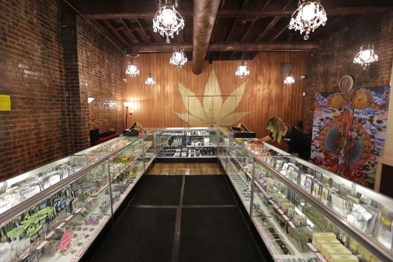 File photo, Dec. 7, 2015, a worker cleans a display case at the Ganja Goddess Cannabis Store in Seattle. On Monday, June 7, 2021, Washington state officials announced that the state's nearly 500 licensed marijuana retailers could begin hosting COVID-19 vaccine clinics and offering a single, free pre-rolled marijuana cigarette to any adult over 21 who receives a shot on-site, but due to federal law and other complications, it's not clear if any of the state's legal pot shops will participate. A current manager at Ganja Goddess said that they would not be participating because they do not have space to host a clinic. CREDIT: Ted S. Warren/AP